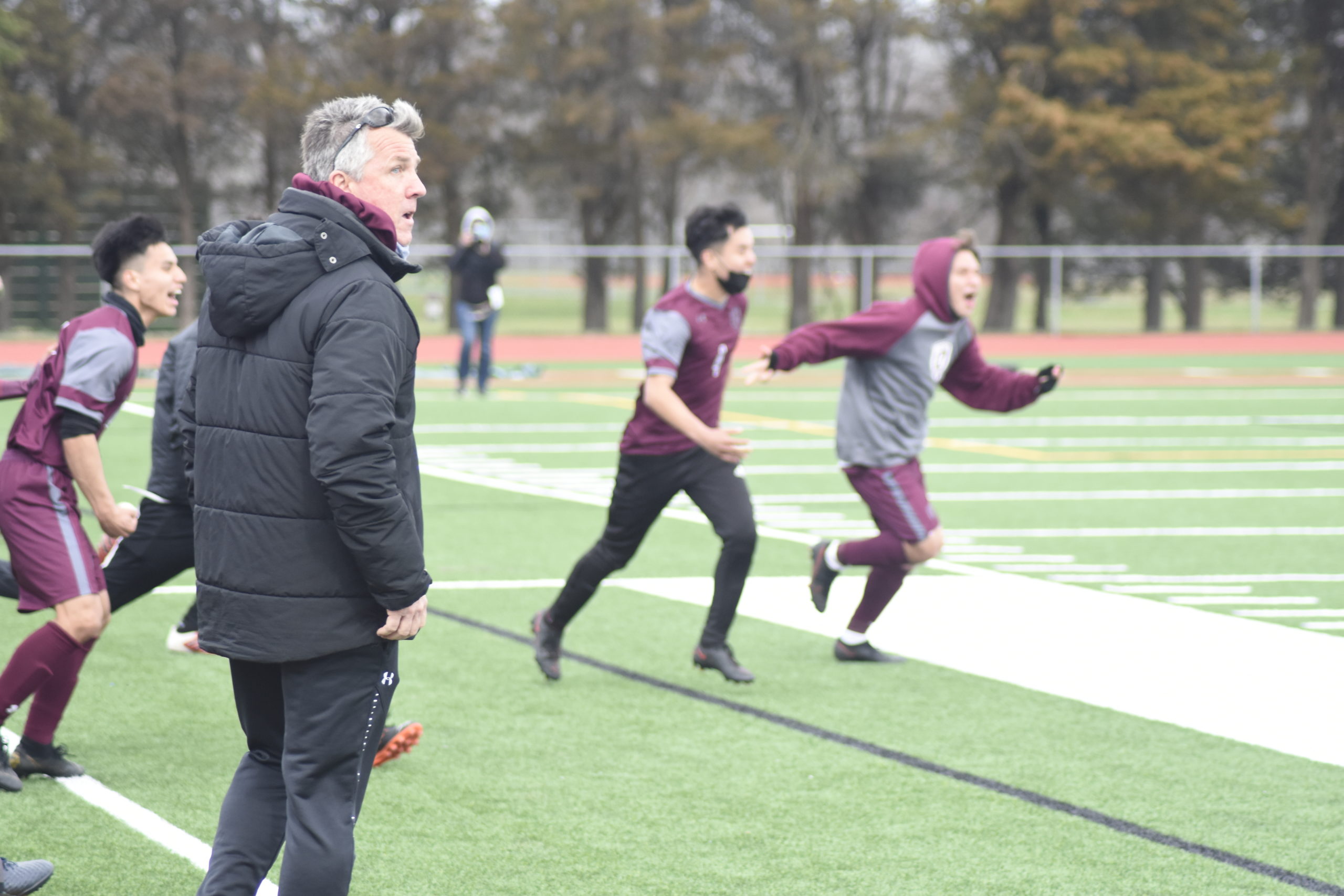 East Hampton head coach Don McGovern looks back at the scoreboard as the final seconds tick and his players run onto the field to celebrate their big 1-0 victory over Amityville on Wednesday.