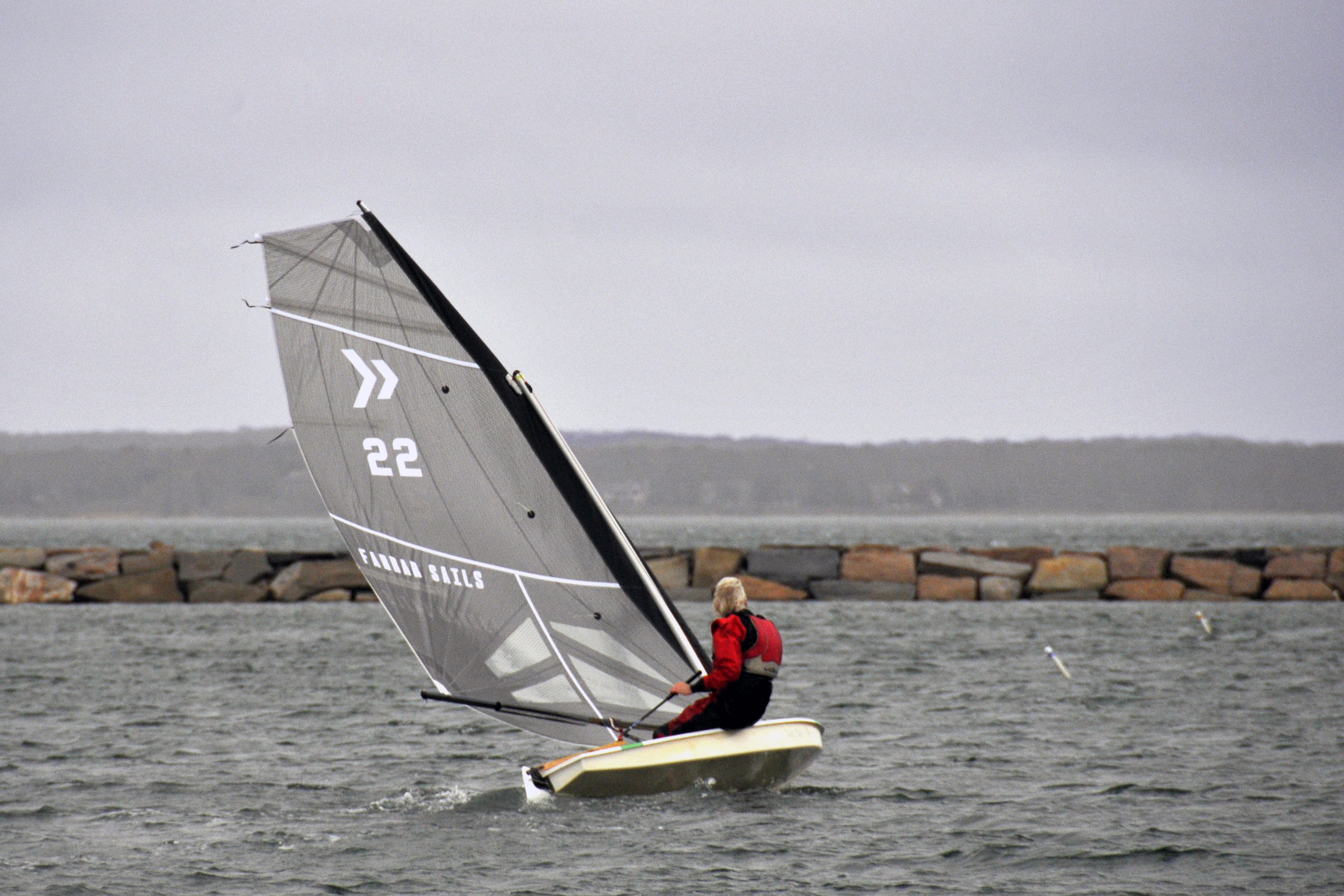 Scott Sandell felt an ardent desire to demonstrate his new black carbon fiber sail to fellow club members, and he did just that. The chase boat covered his every tack and jibe as he careened solo around the inner harbor at breakneck, planning speeds.