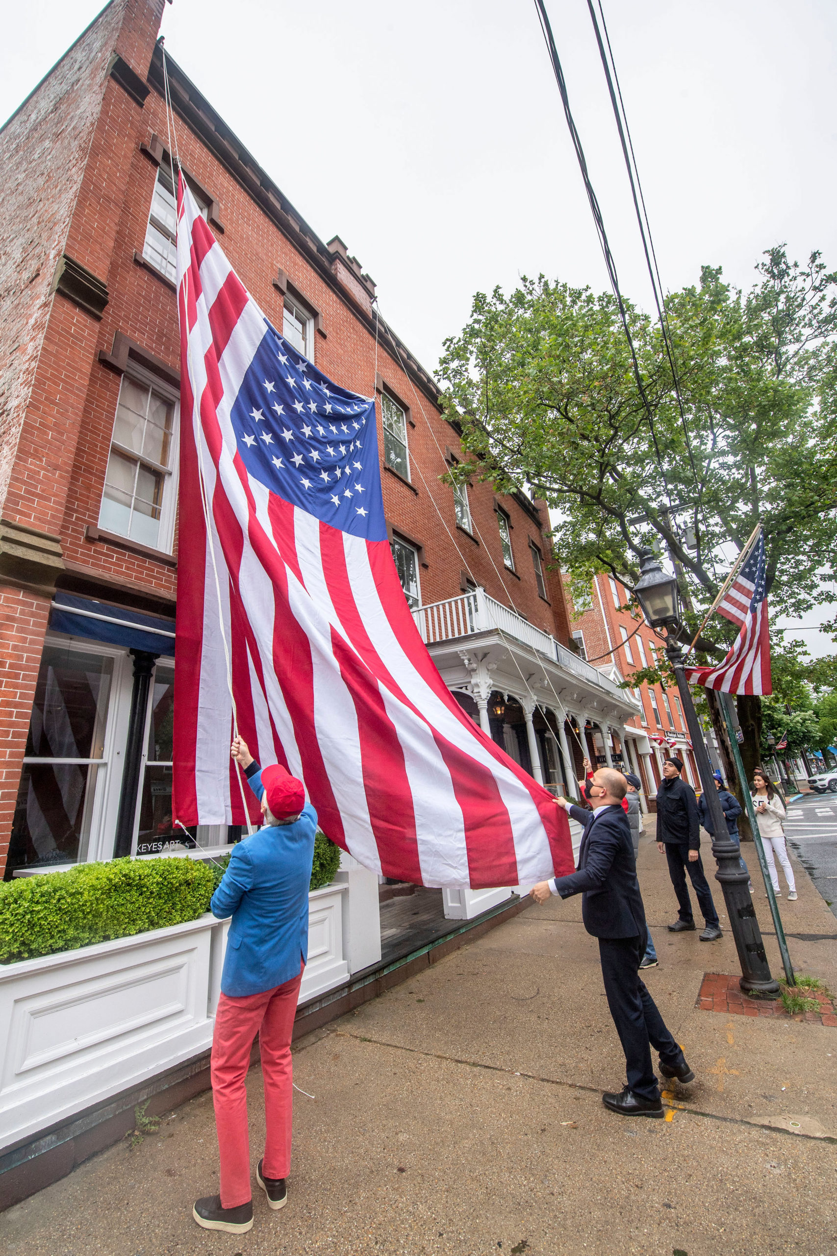 In a long-standing tradition, a large American flag is raised against the American Hotel in preparation for the 2021 Memorial Day parade and ceremonies in Sag Harbor on Monday.  MICHAEL HELLER