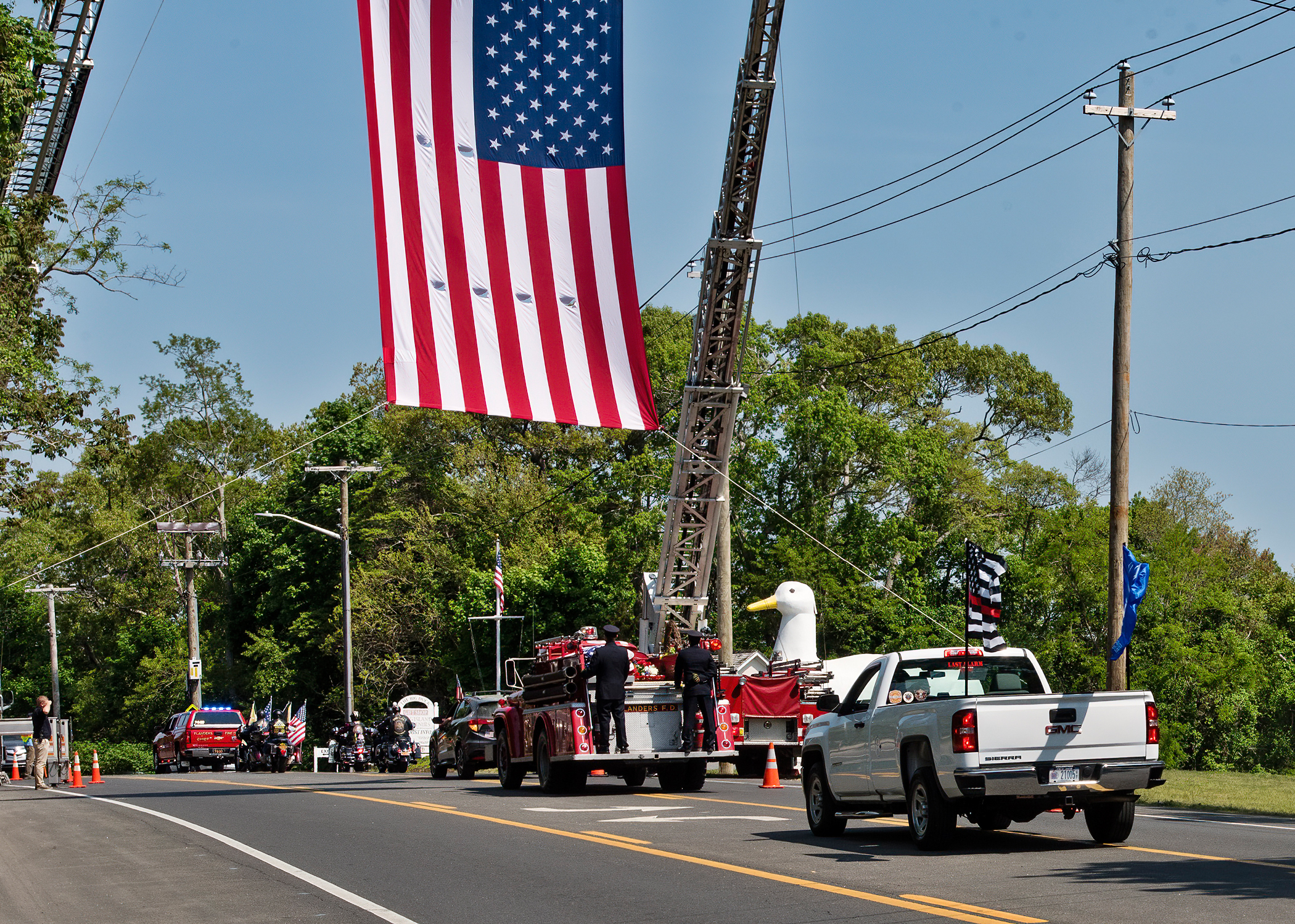 The funeral procession of Flanders Fire Department commissioner and Ex-Chief Frank Belson, Sr., passes under a flag flown by the Riverhead and Westhampton Beach fire departments en route to the Calverton National Cemetery. Chief Belson was an eight year member of the Westhampton Beach Fire Department and a forty-two year member of the Flanders Fire Department.                Courtesy Westhampton Beach Fire Department