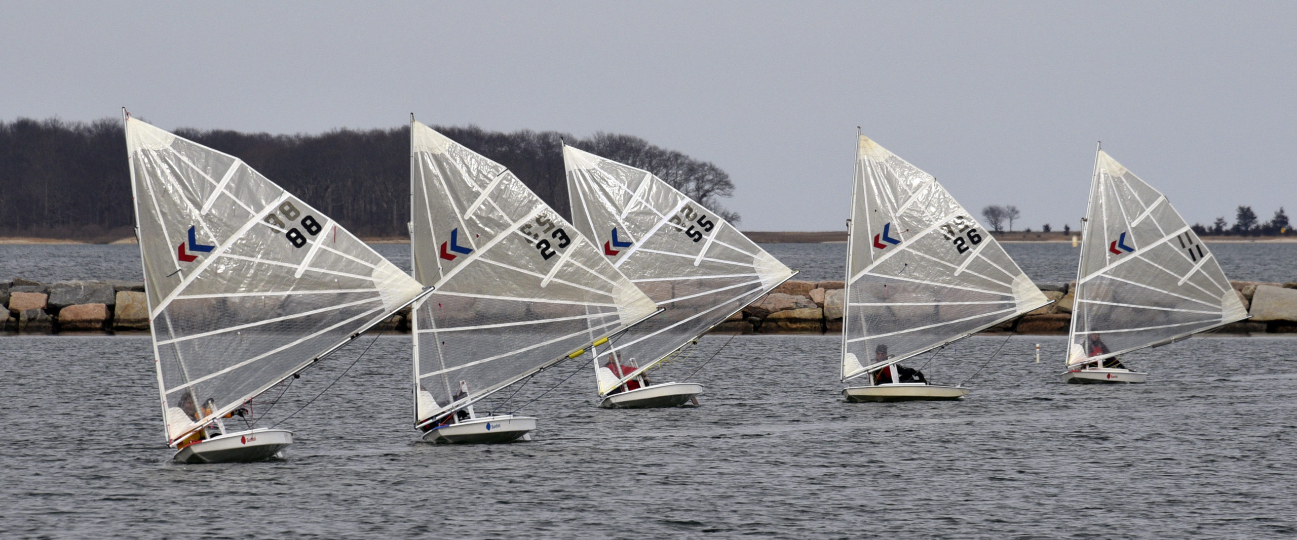 The Breakwater Yacht Club’s “Sunnies” rig-modified Sunfish race most Sunday’s year-round. Like this February 2019 regatta, winter racing has the bone-chilling tagline Frostbite. Pictured here, in the order the skippers finished, from left: Derrick Galen, Gloria Maroti Frazee, the club’s sail designer Scott Sandell, Julian Shapiro and Brenna Gilroy.        MICHAEL MELLA