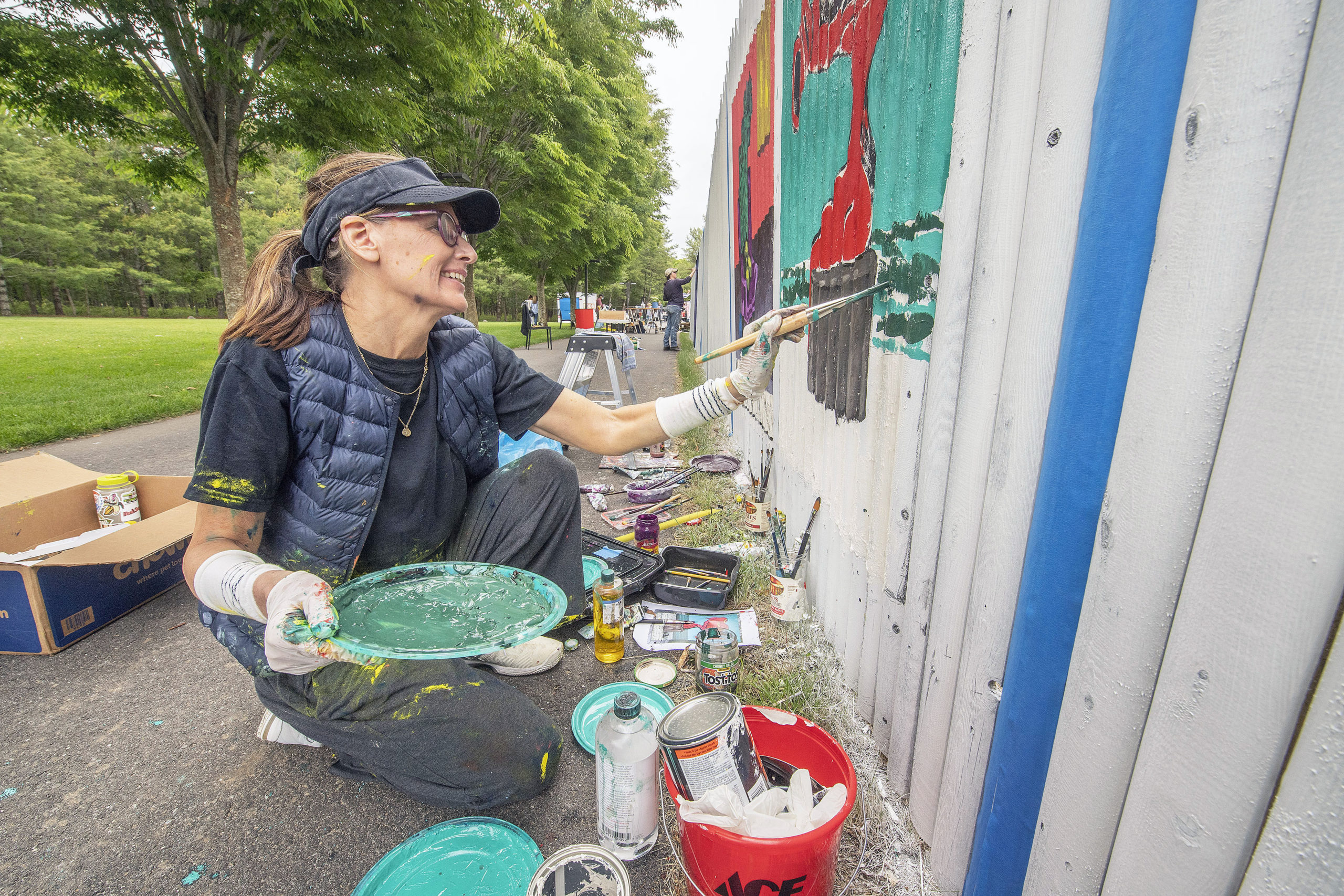 A paint-covered Lori Campbell works on her entry during the Live Mural and Graffiti Competition at The Clubhouse on Saturday, June 12.