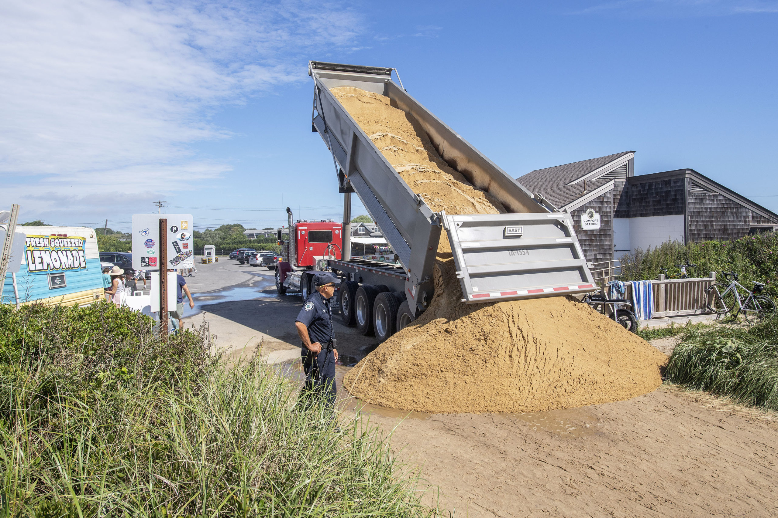 As an East Hampton Town Marine Patrol officer looks on, an East Hampton Town Highway worker dumps a load of sand at the entrance to Ditch Plains Beach in Montauk in preparation for Hurricane Henri on Saturday,    MICHAEL HELLER