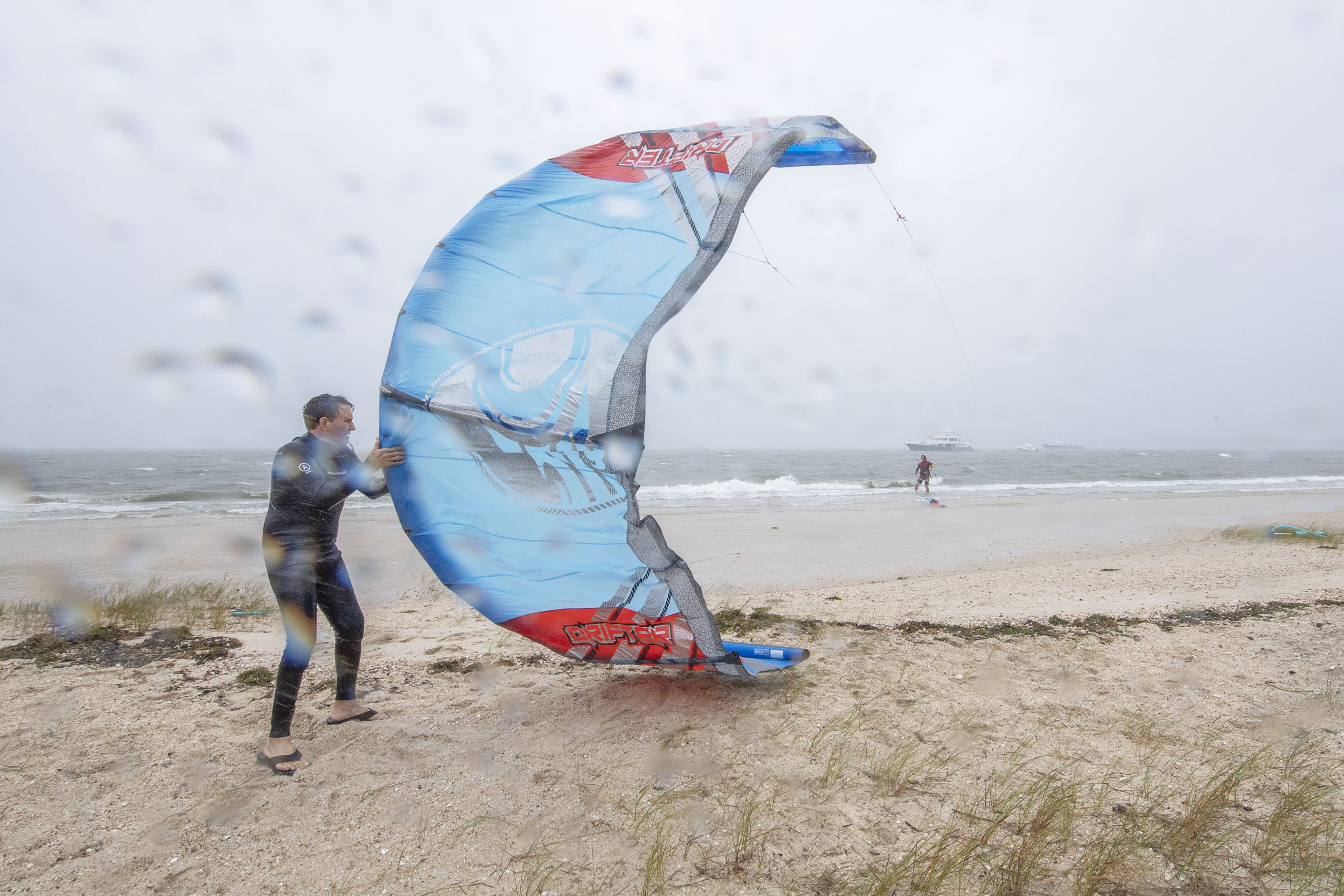 A fellow kiteboarder helps Ben Miller launch his kite in 30-mph wind gusts and rain as he goes kiteboarding along Long Beach in Sag Harbor during Tropical Storm Henri on Sunday.   MICHAEL HELLER
