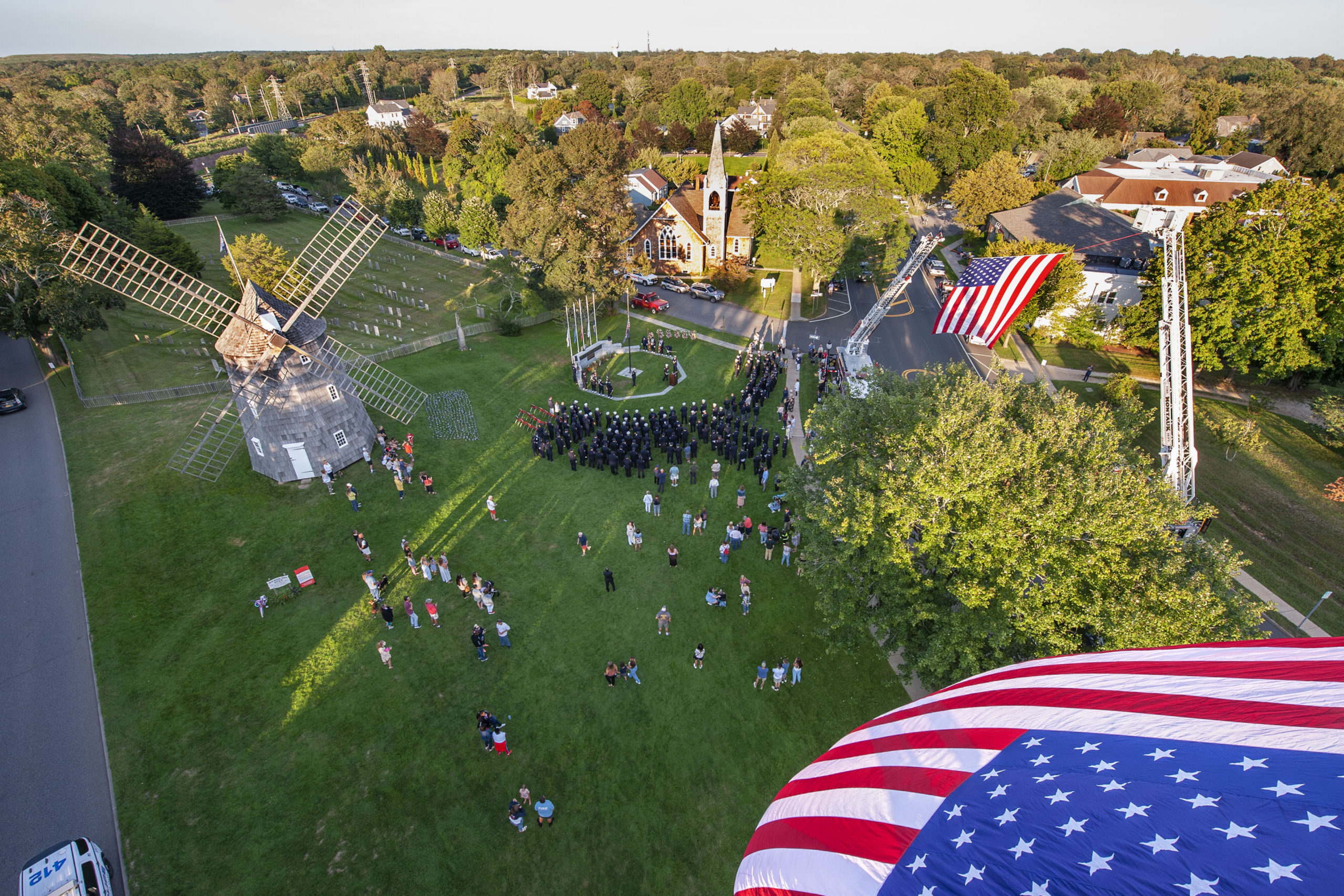 Large American flags fly over the East Hampton Village Green and Montauk Highway - courtesy of the East Hampton,  Sag Harbor, Bridgehampton and Montauk Fire Departments - during a ceremony commemorating the 20th anniversary of the attack on the World Trade Center, held on the Village Green in East Hampton and attended by 11 different East End fire, police and EMS agencies on Saturday afternoon.