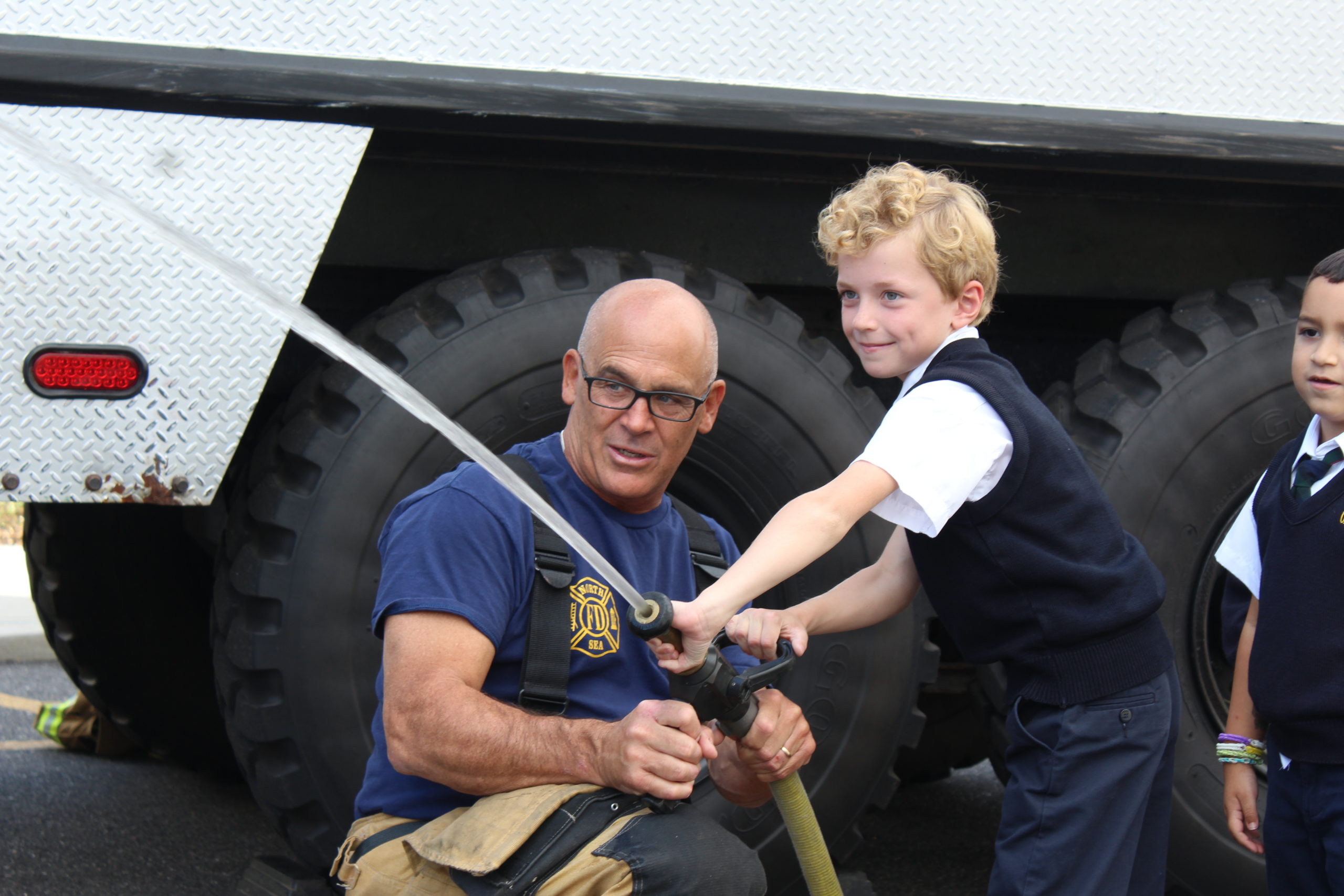 Our Lady of the Hamptons School second-grader Oliver Fulweiler gets instruction on using the fire house from fireman Mark Hannan.