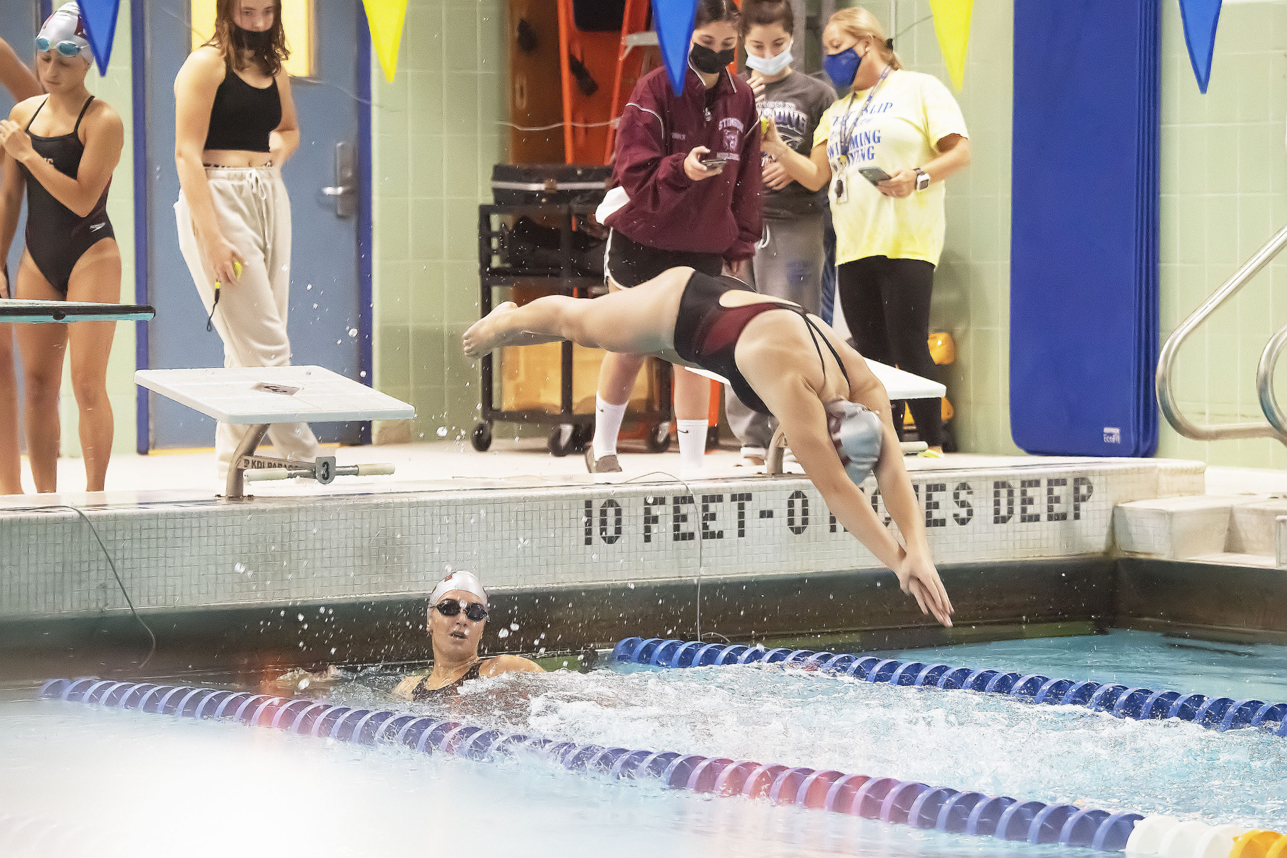 As Camryn Hatch looks on, Lily Griffin dives to begin the second leg of the 200-yard medley relay.