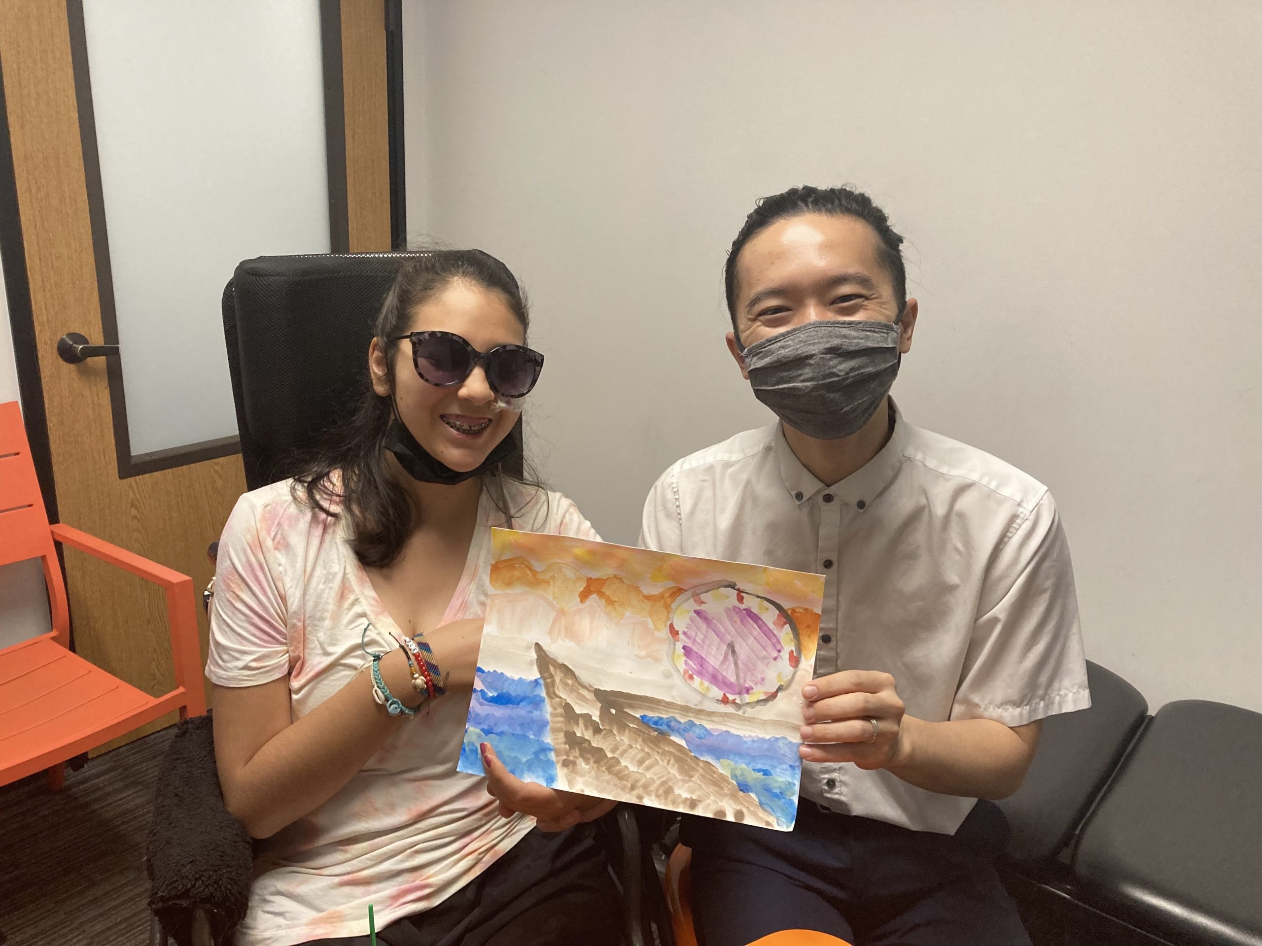 Bella Adlah and Dr. Naoya Ogura with her painting of the Santa Monica Pier at Re+active Physical Therapy in California.