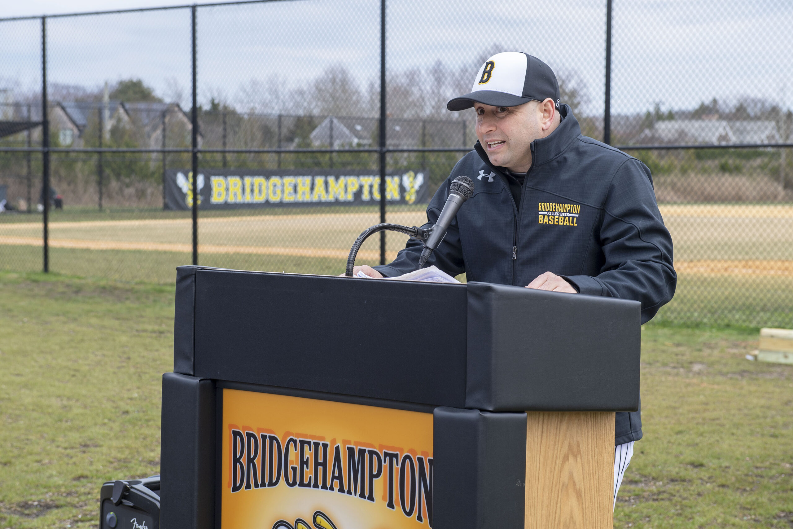 Bridgehampton School Athletic Director Mike DeRosa addresses the crowd during a dedication ceremony prior to the start of the baseball game between the Bridgehampton Killer Bees and the Shelter Island Islanders on Tuesday.   MICHAEL HELLER