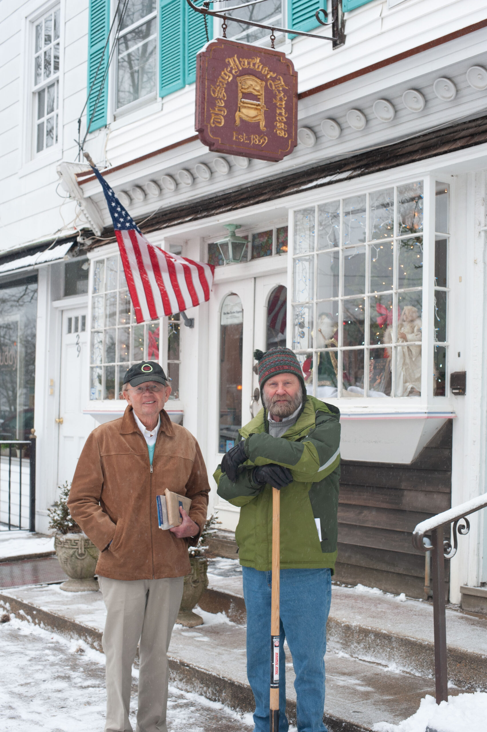 Gardner “Pat” Cowles and Bryan Boyhan in front of the Sag Harbor Express office during a snow storm in 2013.     MICHAEL HELLER