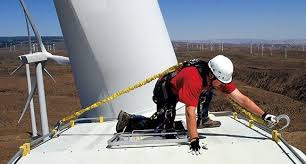 A wind turbine technician latching on to the top of a wind turbine nacelle before performing maintenance duties.