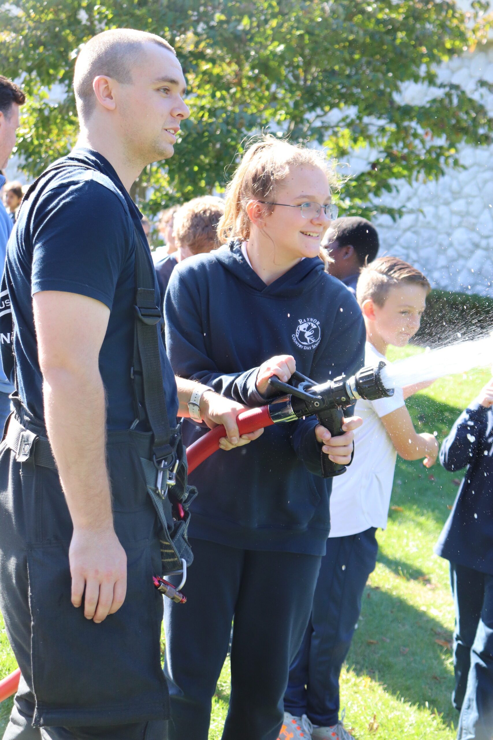 The Eastport Fire Department visited Raynor Country Day School on October 22 to talk about fire safety and the new equipment the department has in its fleet.  Sixth-grader Emily Thullen takes a moment at the hose with the assistance of a volunteer firefighter.  COURTESY RAYNOR COUNTRY DAY SCHOOL