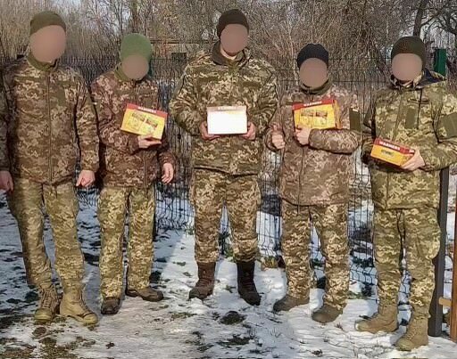 Ukrainian soldier, their faces obscured,  with boxes of feet and hand warmers they received from American donors. COURTESY NADIA ERNESTUS