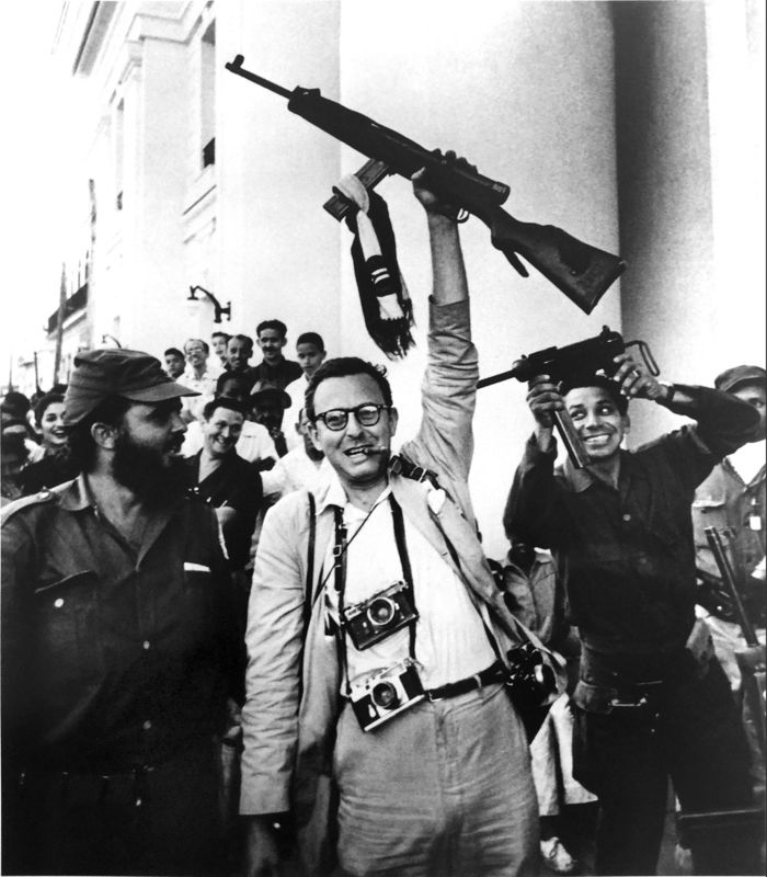 Photographer Burt Glinn, holding a gun in the air, on the other side of the lens in Cuba. 