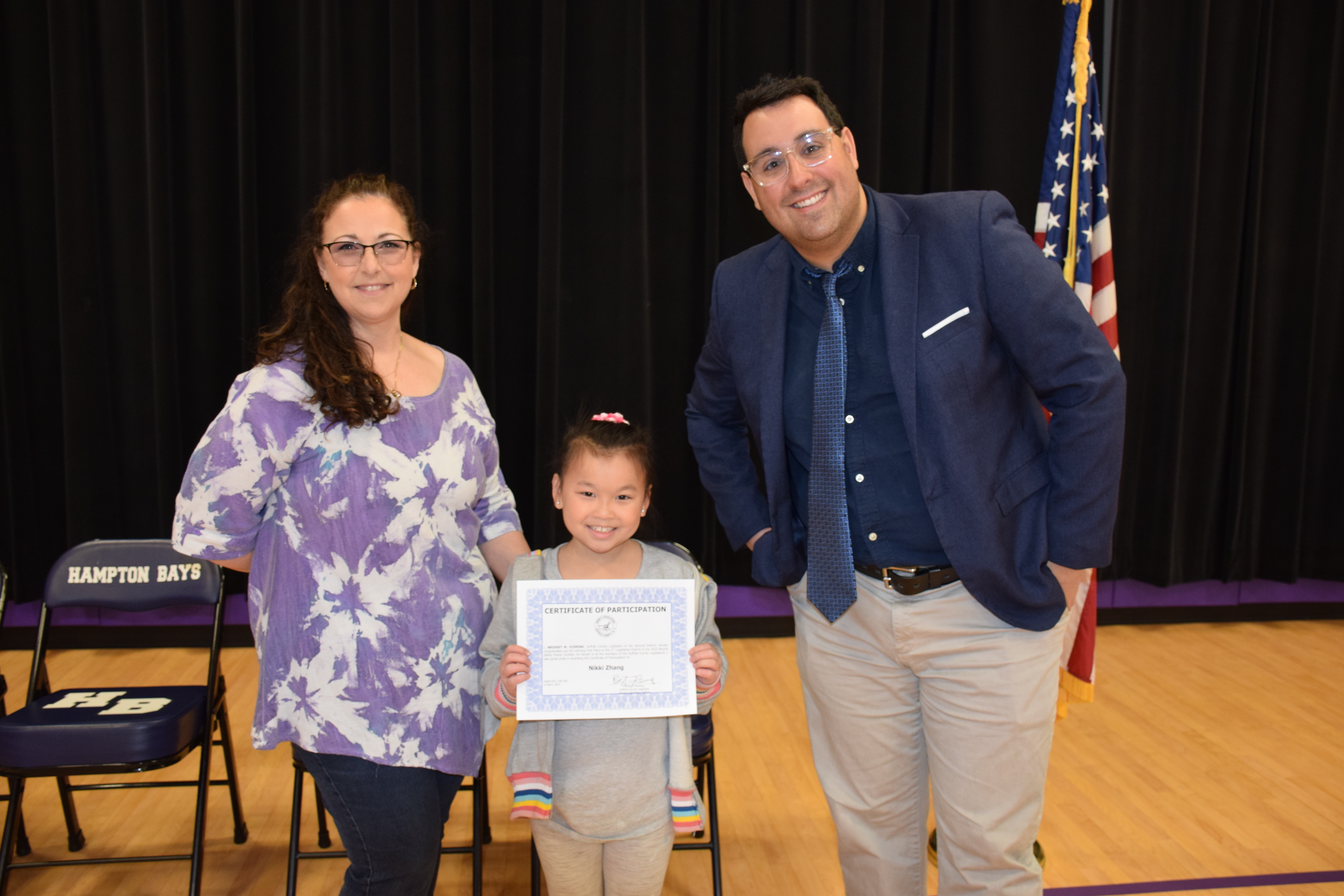 Hampton Bays Elementary School third-grader Nikki Zhang was recently awarded first place in the Suffolk County Legislature’s Bike Safety Poster Contest. Zhang was one of 73 Hampton Bays students to participate in the contest and her work will be displayed at Legislator Bridget Fleming’s office. All students received a certificate of participation from Legislator Fleming during a ceremony on April 25. From left, Hampton Bays Elementary School art teacher Debra McDowell, Nikki Zhang and Dr.
Michael Lasilli, representative for Suffolk Country Legislator Bridget Fleming. COURTESY HAMPTON BAYS SCHOOL DISTRICT