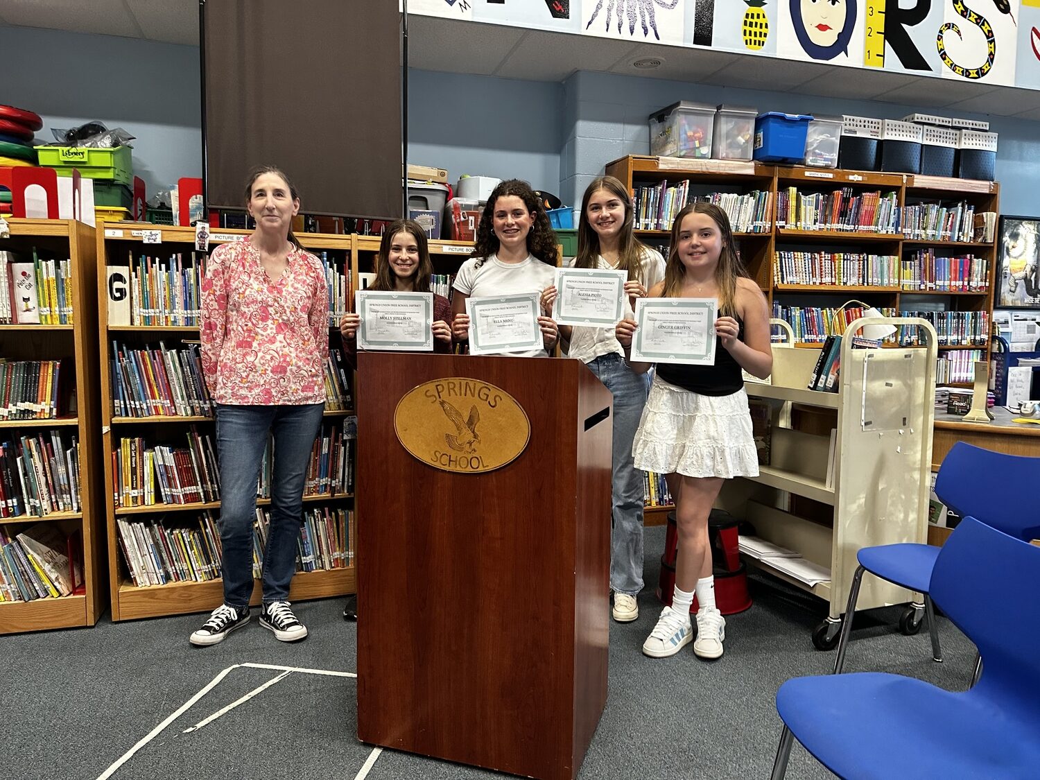 Springs School Board of Education President Barbara Dayton at last Tuesday’s board of education meeting where the board honored their salutatorian and valedictorians from the eighth grade class. (Left to right) Molly Stillman is the class salutatorian, with Ella Menu, Alessa Picco and Ginger Griffin sharing top honors as the class valedictorian. Ella Menu was also recognized at Tuesday night’s meeting for being the first place winner in the annual eighth grade speech competition for her speech on “Stop the Stigma,” a discussion on mental health. Alessa Picco placed second in that contest for her talk on “Their Silent Suffering,” about rape and the criminal justice system, and Valentina Arango placed third for her talk, “Fly Free,” about women’s rights in Saudia Arabia and around the world.