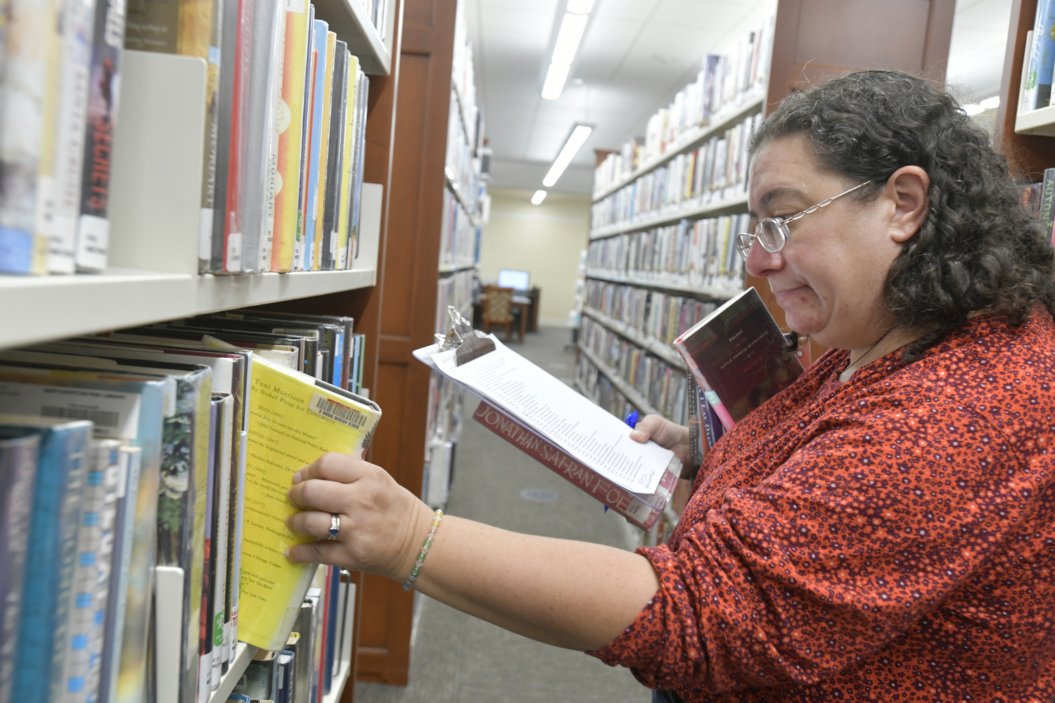 Mara Zonderman, the head of reference and adult services, scans the shelves on Friday afternoon, moving from department to department with a list over 500 titles long, pulling picture books and chapter books, children’s graphic novels, young adult reads, adult fiction and non-fiction alike.   DANA SHAW