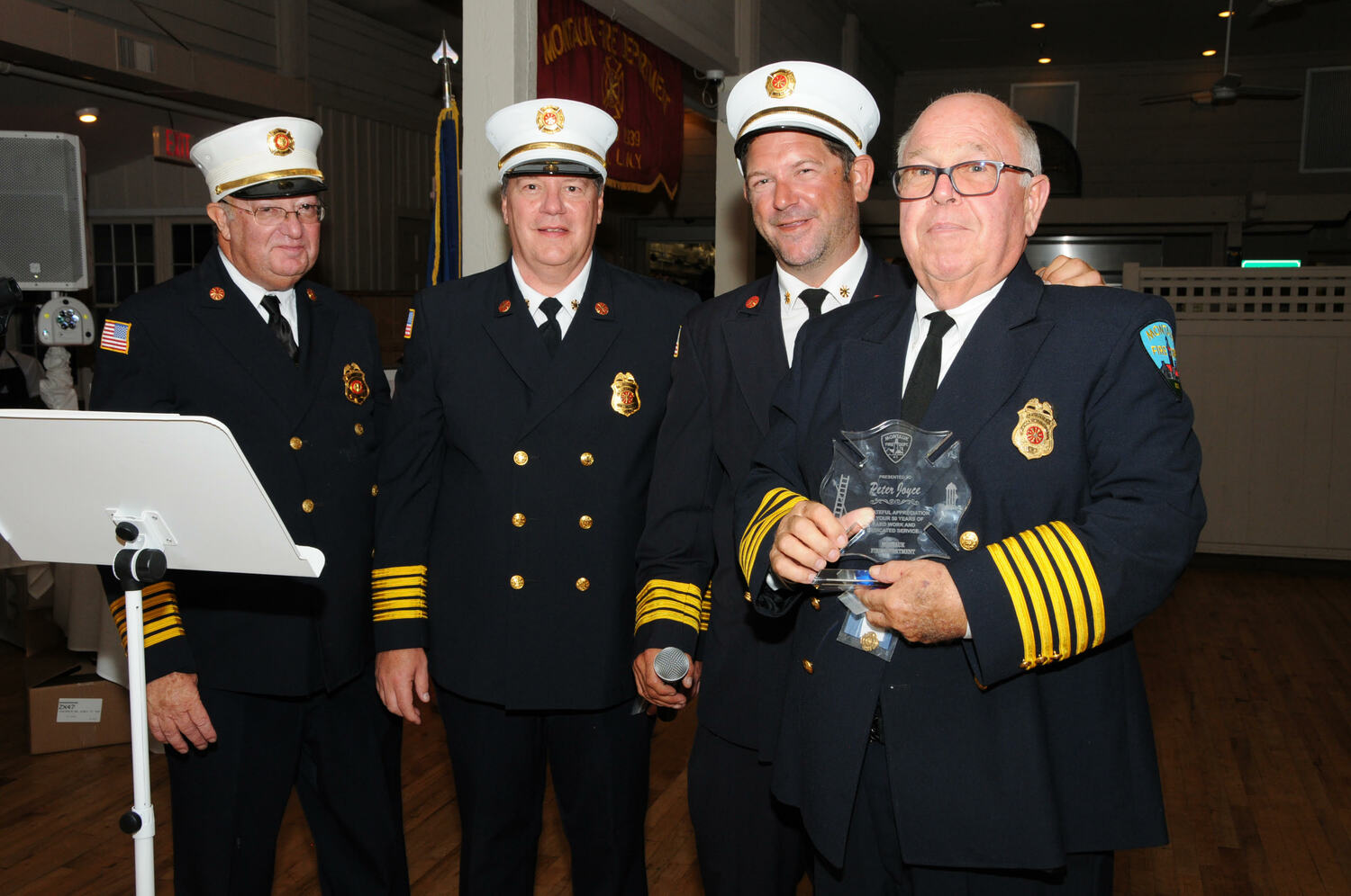 Montauk Fire Department Second Assistant Chief John McDonald,  Chief Ken Glogg, and First Assistant Chief Peter Joyce, Jr. present Ex-Chief Peter Joyce with his 2023 