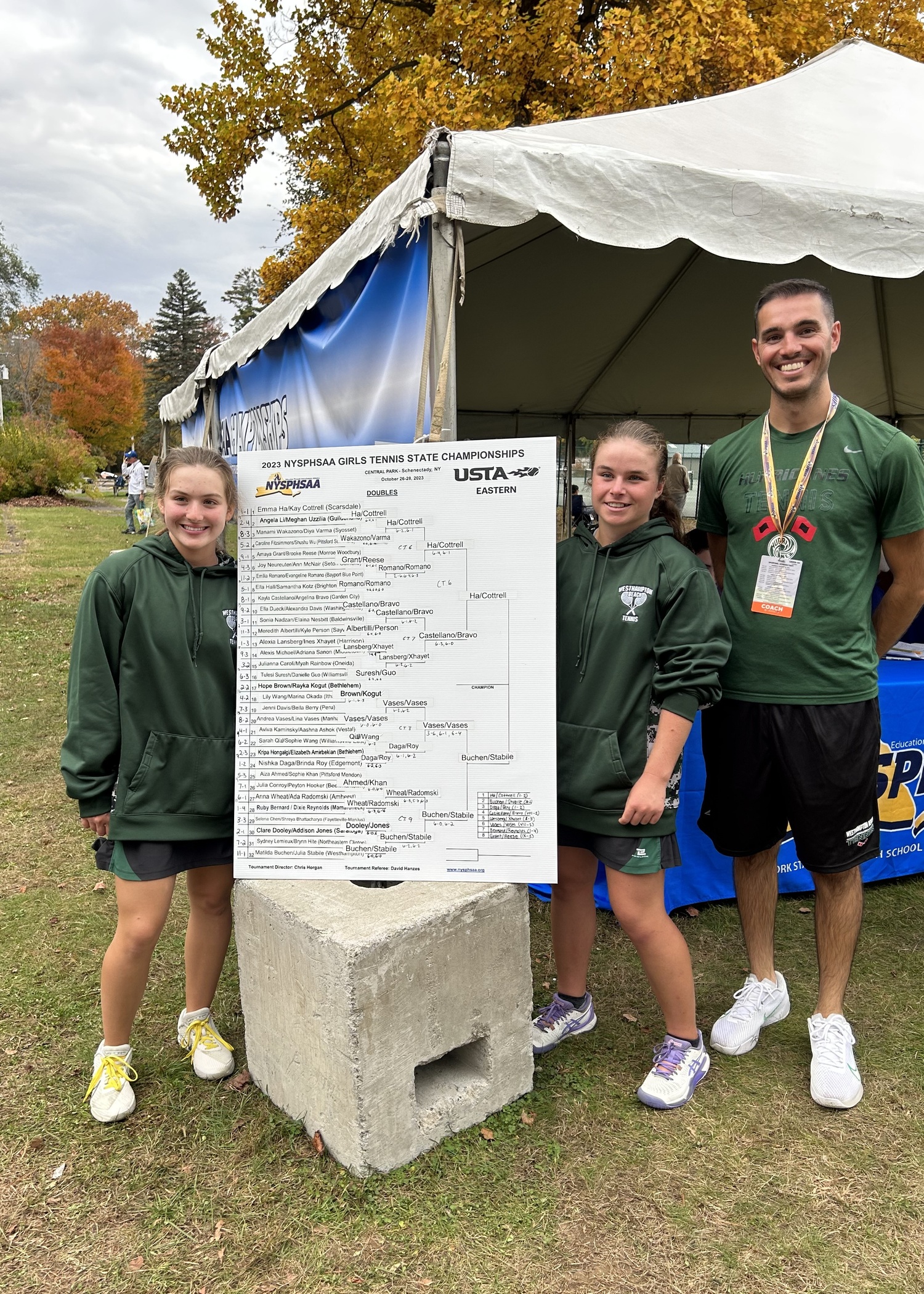 Westhampton Beach's doubles duo of Matilda Buchen and Julia Stabile show off their winning bracket with head coach Matt Reed after their state championship tournament win.