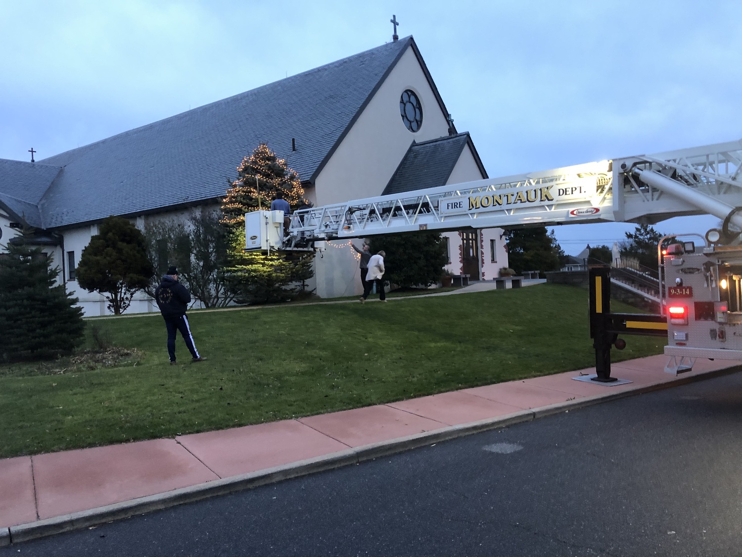 A crew and ladder truck from Montauk Fire  Department made a stop at St Therese Church to hang the lights on the top of the church’s perennial Christmas tree late Friday afternoon.  COURTESY T.E. MCMORROW