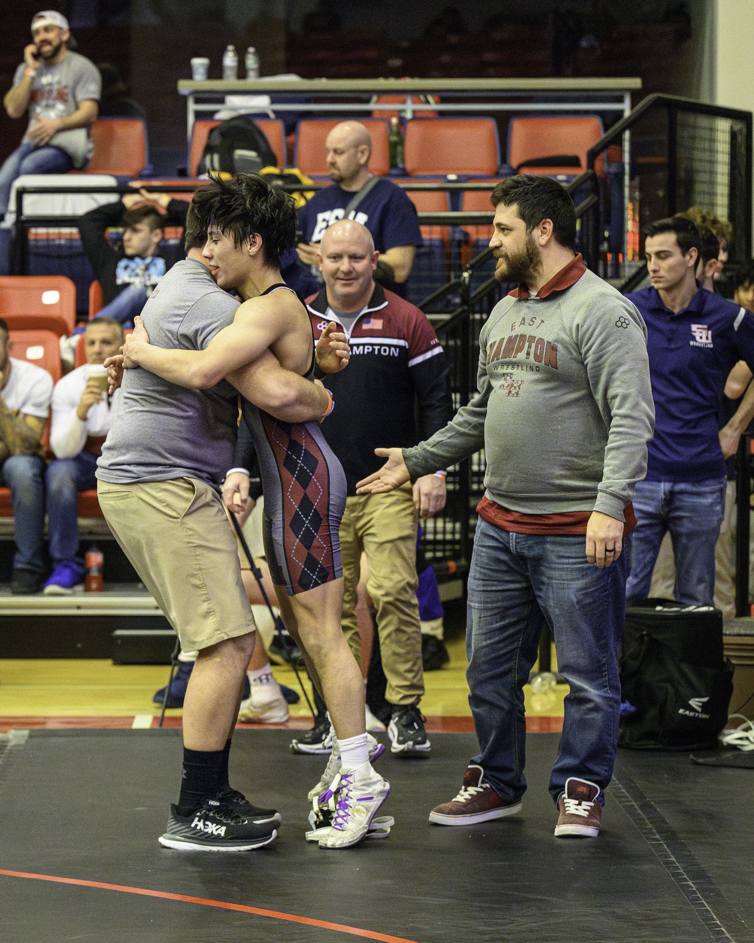 East Hampton junior Juan Roque gets a hug from head coach Ethan Mitchell and is congratulated by his assistant coaches after winning his quarterfinals match on Saturday.   MARIANNE BARNETT