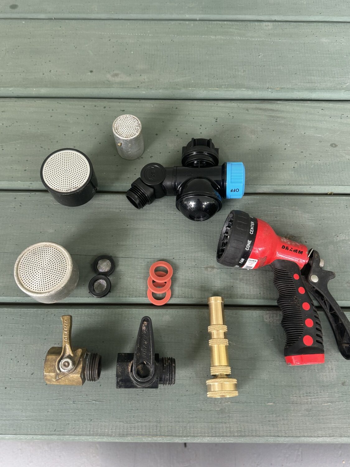A collection of watering tools. On the bottom are a brass control valve (left) which will last for years and is repairable. The plastic valve to the right is easily broken. To the right is a brass 4-inch twist nozzle that goes from a fine spray to a stream with a twist of the barrel. Top left are three Dramm watering heads. The metal is preferred to the plastic as they last longer. To the right is a new gadget that allows you to run a hose off your hose bib and an on/off to control the perforated output for washing your hands or tools.  In the center are hose washers with screens, and to the right are standard (preferred) rubber washers. On the far right is a hose-end watering head with 10 settings from a fine spray to a stream and all in between.  These tend to break easily and make a mess when in use. ANDREW MESSINGER