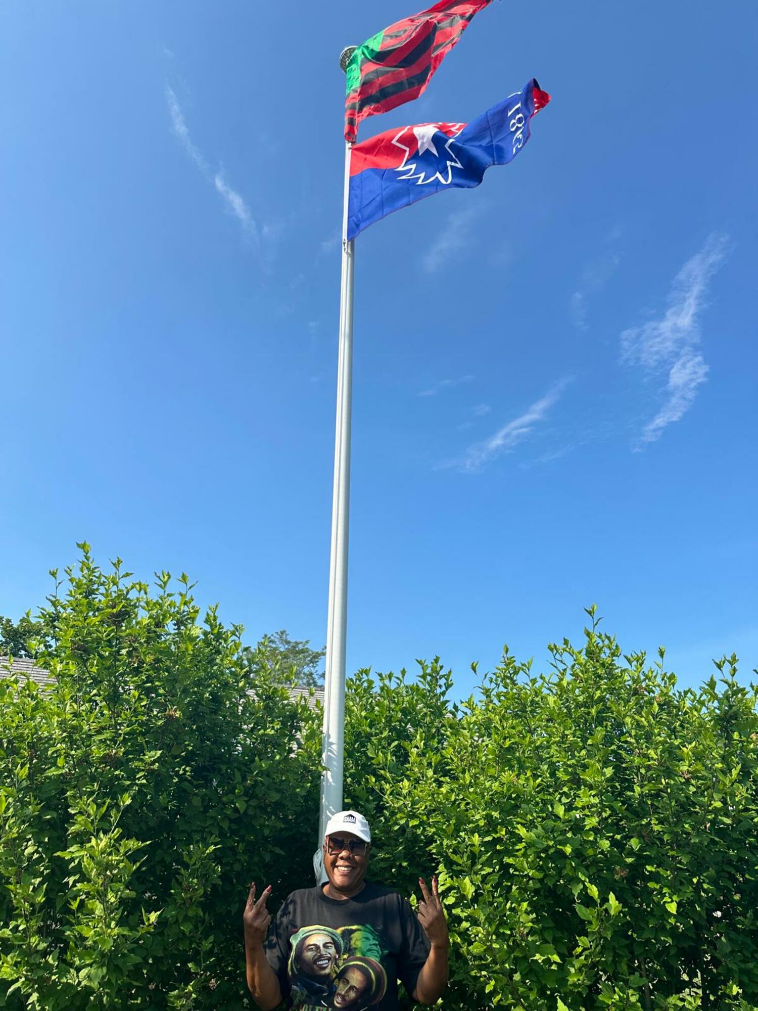 The red, black and green Pan-African flag, also known as the Marcus Garvey flag, and the red, white and blue Juneteenth flag, are now flying at the Southampton African American Museum. Standing in front of the flagpole is SAAM Executive Director Brenda Simmons. COURTESY SAAM