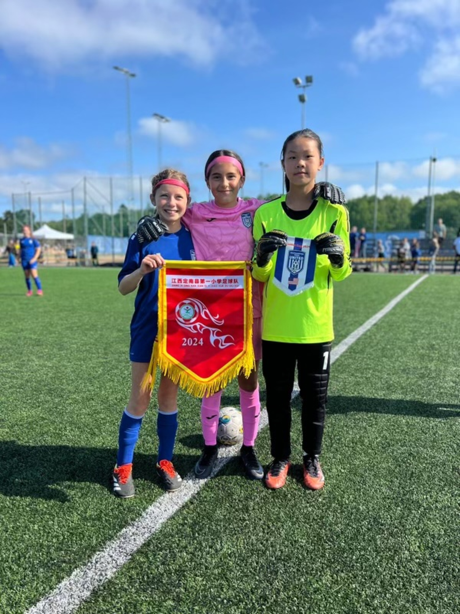 From left, Mia Rybak and Gabby Jimenez, members of the 2012 team, exchanging team banners with a player from China.