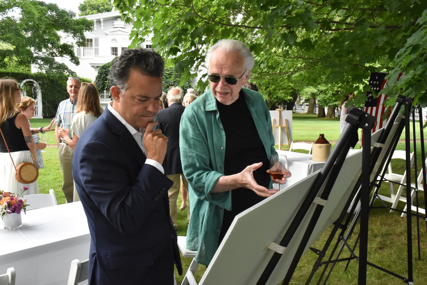 Randy Croxton and John Avlon examine posters outlining the Sag Harbor Historical Museum's quest to identify the remains of a British fort that occupied much of the Old Burying Ground during the Revolutionary War at the museum's summer party on Saturday. STEPHEN J. KOTZ