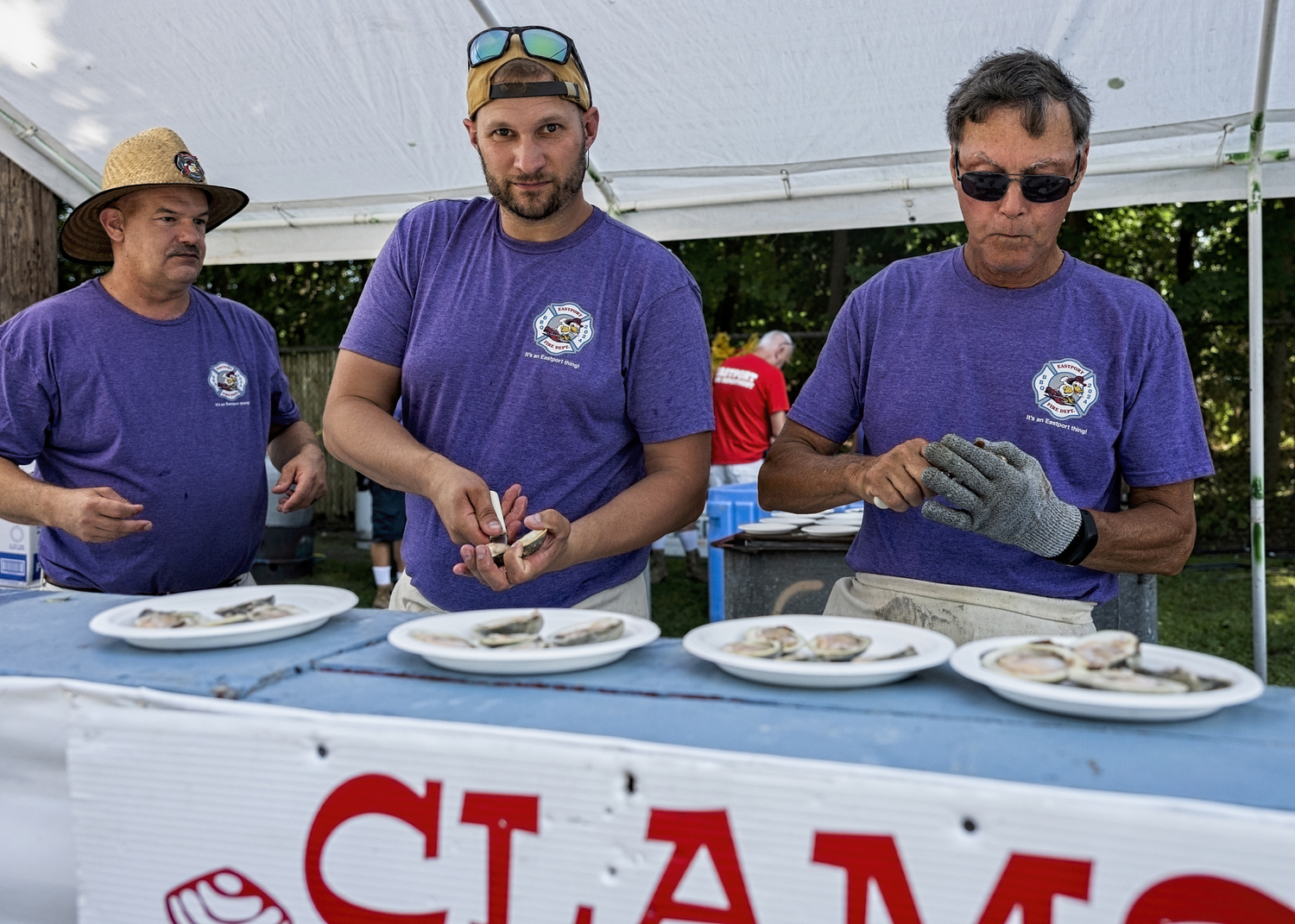 Bradley Dunn, Rob Navratil, and Paul Massey shuck clams at the Eastport Fire Department's Chicken and Lobster Barbecue on August 3.    COURTESY WESTHAMPTON BEACH FIRE DEPARTMENT