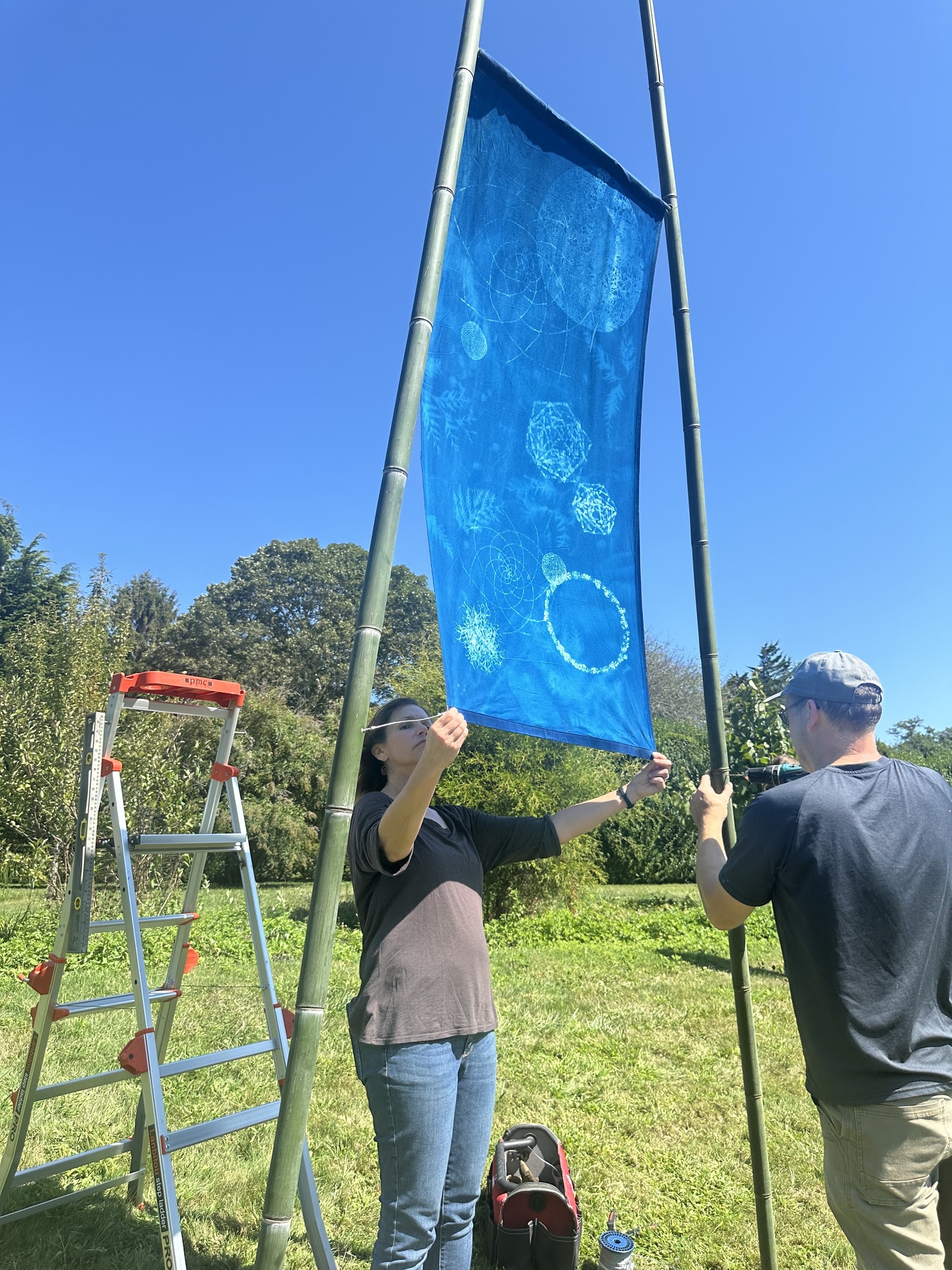 Artist Andrea Cote and her husband, Pierre, hanging her cyanotype banners at Bridge Gardens on September 9. ANNETTE HINKLE