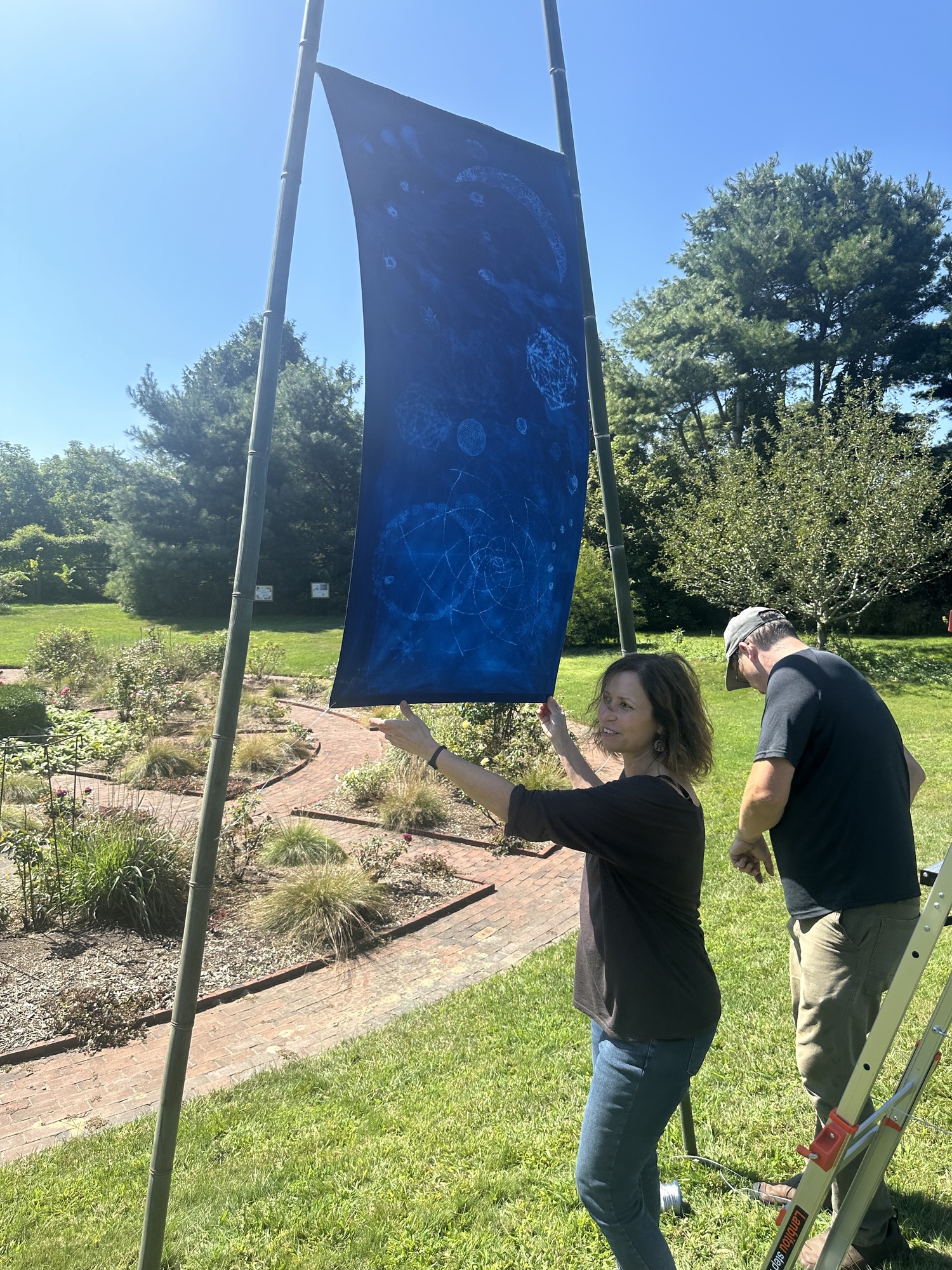 Artist Andrea Cote and her husband, Pierre, hanging her cyanotype banners at Bridge Gardens on September 9. ANNETTE HINKLE