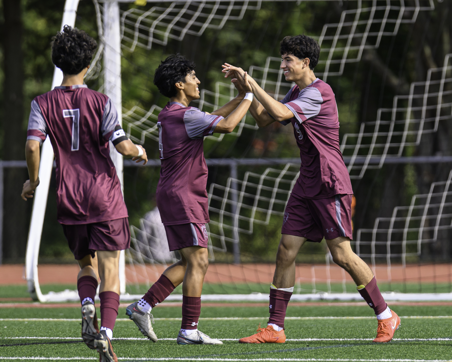 Senior forward Ariel Garcia, midfielder Jonathan Armijos and forward Nolan Serrano celebrate Armijos' late goal to ice it for East Hampton. MARIANNE BARNETT