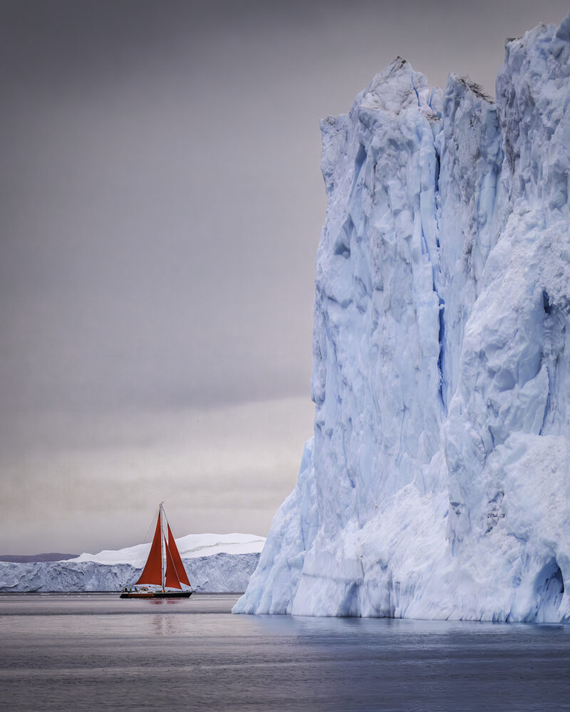 An iceberg dwarfs a sailboat. MARIANNE BARNETT