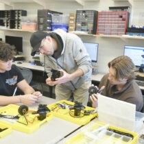 James Dudley, instructor Eric Pflug and Konstantine Lazarakis work on the bots.  DANA SHAW