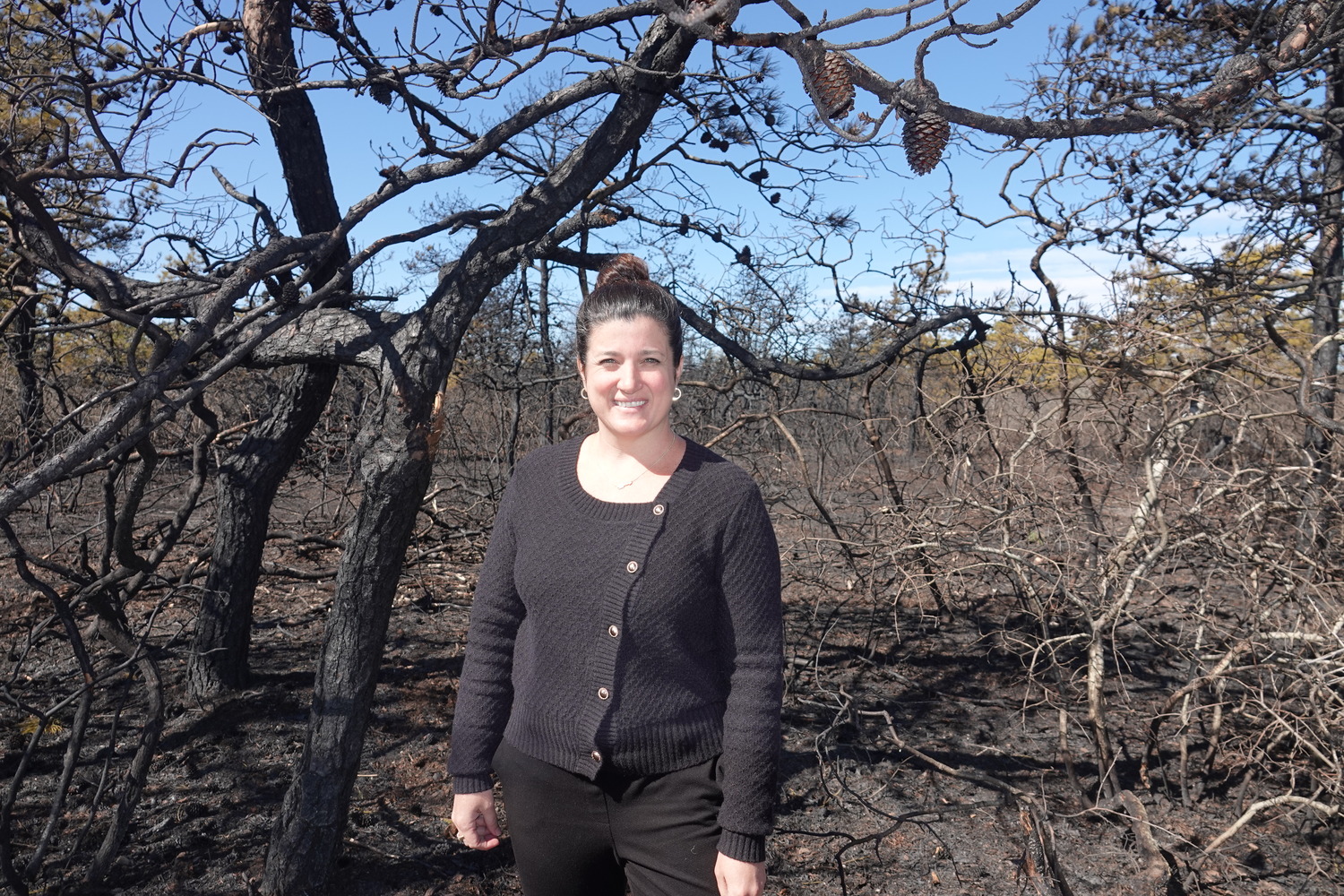 East End Hospice Executive Director Mary Crosby in the charred woods outside the Hospice office building in Westhampton. Flames wafted over the organization's offices, and set a storage container and dumpster on fire, but firefighters were able to save the building from destruction. MICHAEL WRIGHT