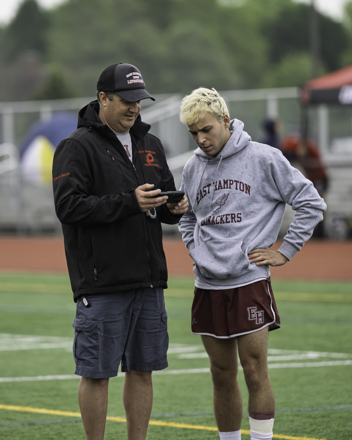 East Hampton boys track head coach Sean Knight, left, going over some footage of Abe Stillman in the pole vault on Saturday.   MARIANNE BARNETT
