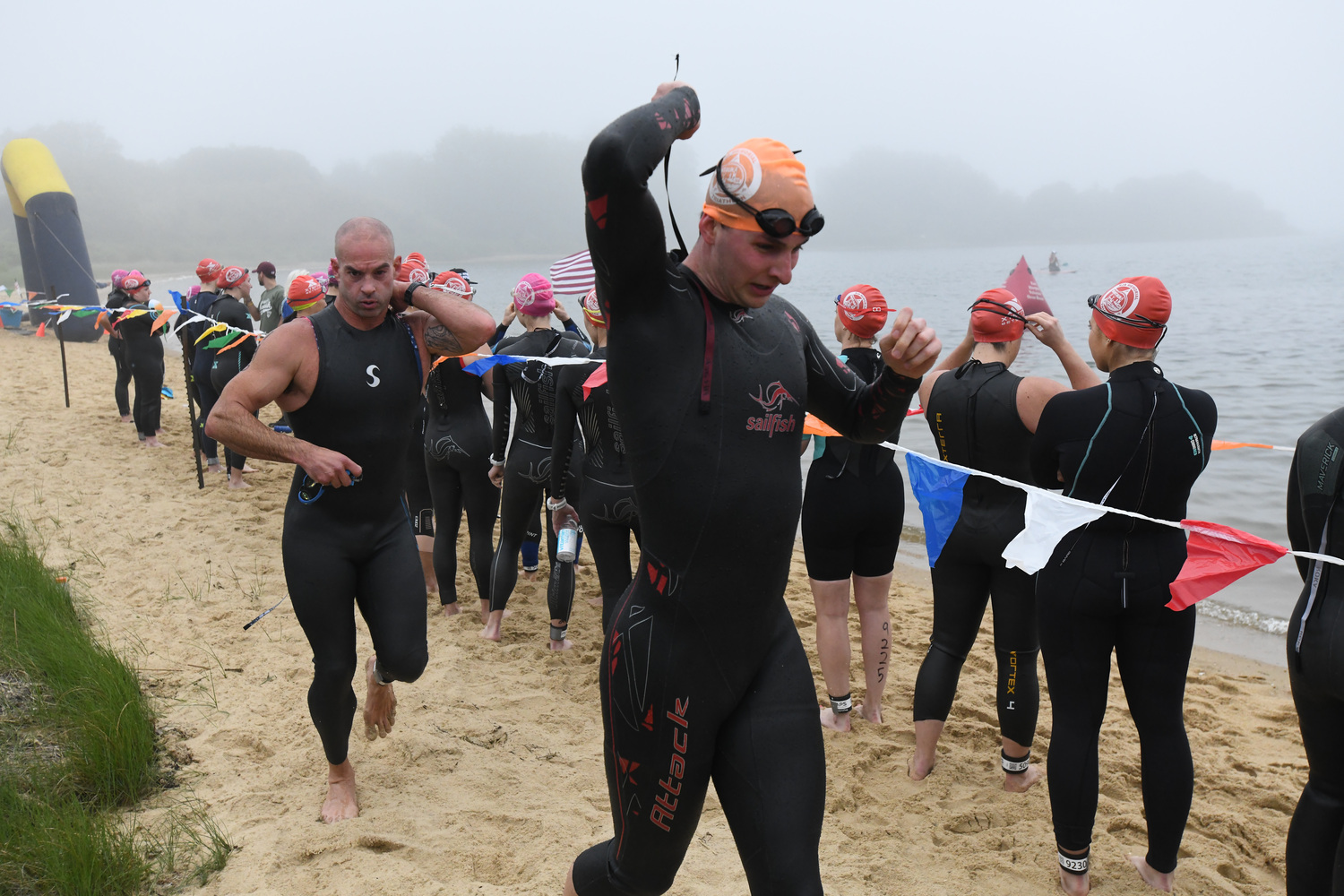 Triathletes make their way out of the water at Lake Montauk while others wait to get in at the Robert J. Aaron Mighty Montauk Triathlon on Saturday morning.  DOUG KUNTZ