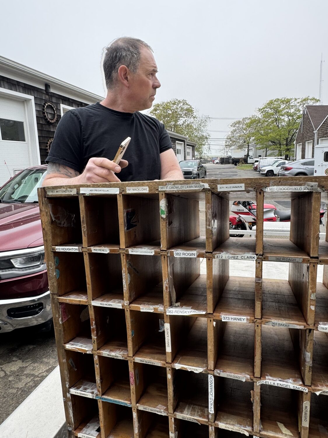 Metal craftsman James DeMartis outside his East Hampton studio with one of the wooden shelves that contained the postal boxes at the old Sagaponack post office. PETER BOODY
