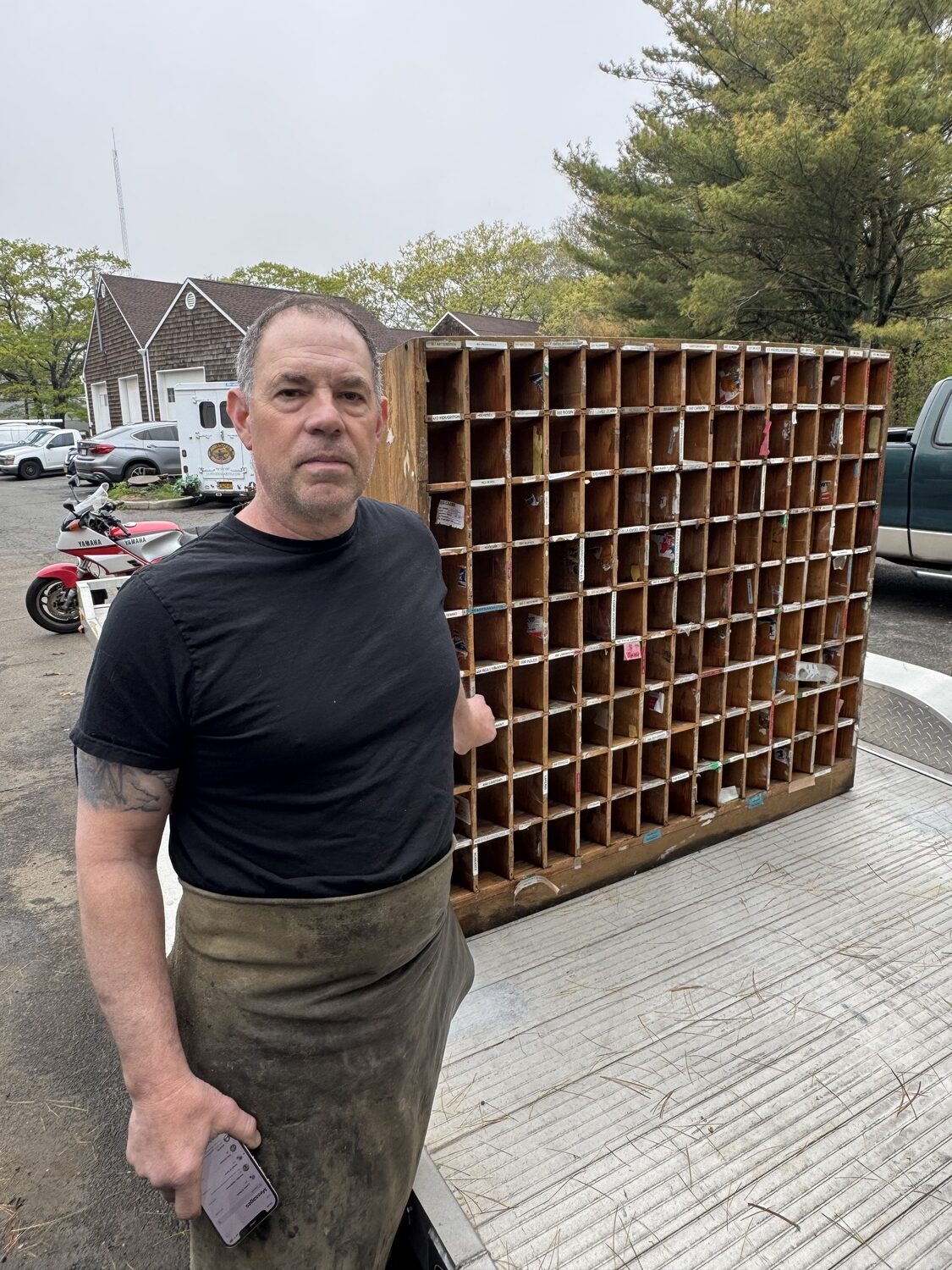 Metal craftsman James DeMartis outside his East Hampton studio with one of the wooden shelves that contained post office boxes in the old Sagaponack Post office. PETER BOODY