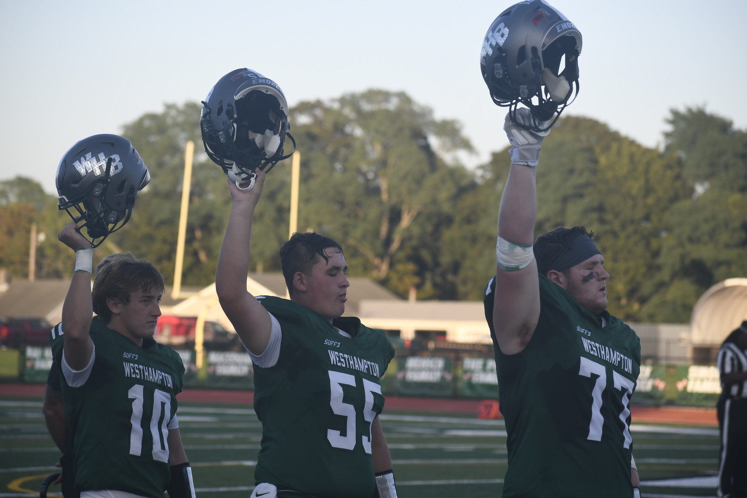 Nate LoGelfo, Ben Magee and J.P. Peters raise their helmets during the national anthem on Friday.  DREW BUDD