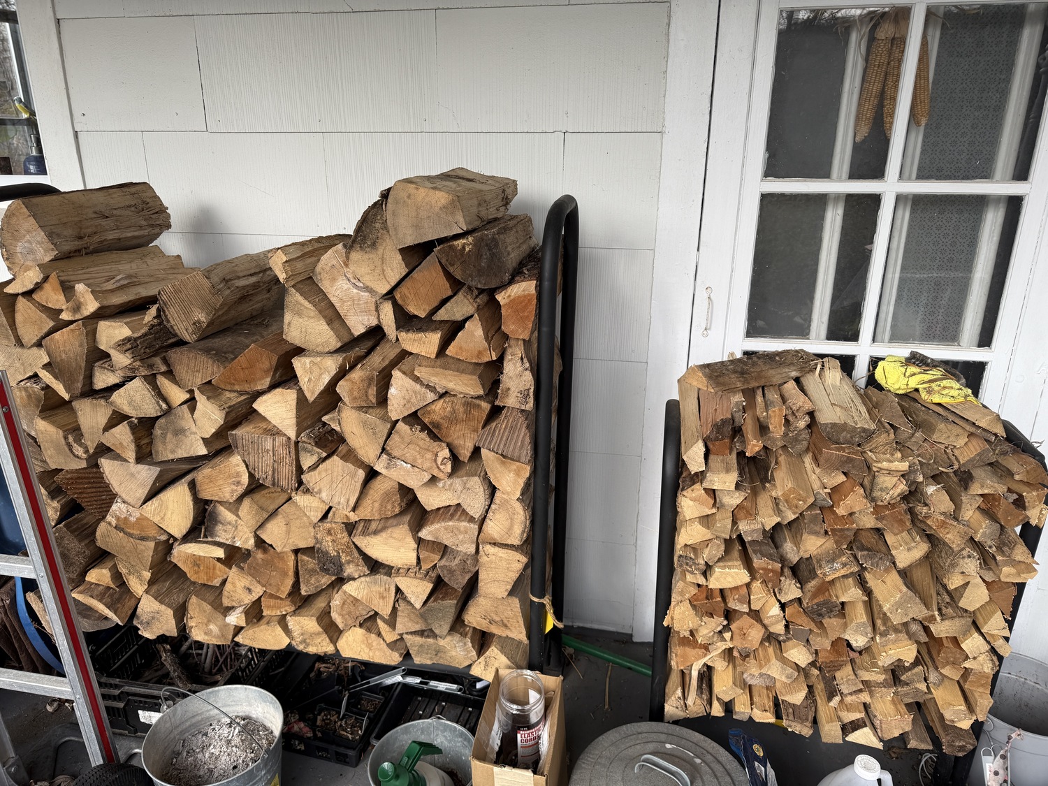 Cordwood should never be stacked against a house, but here is a rack of split wood, left, and a smaller rack of kindling, right, for starting a fire. The rack holds enough wood for a six-to-eight-hour fire in our Lopi stove. In the middle of winter, one rack will last about four or five nights until the wood has to be replaced from the cordwood 20 feet away in the yard. The ashes, lower left, always go into a metal pail and never on a wood surface until the ashes are cold. ANDREW MESSINGER